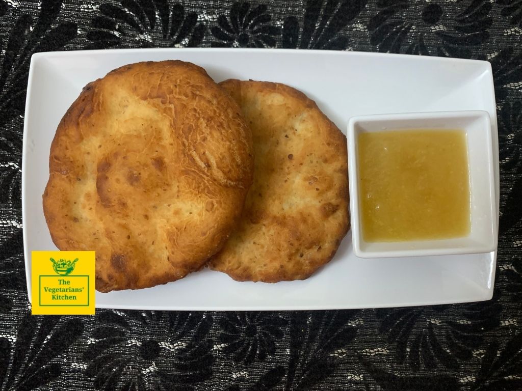 A top shot of two vegan mekici served with apple jam on a white plate against a black background.